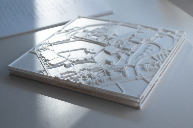 A white tactile map of UTM campus with exhibition sites and Braille on top of a white table.